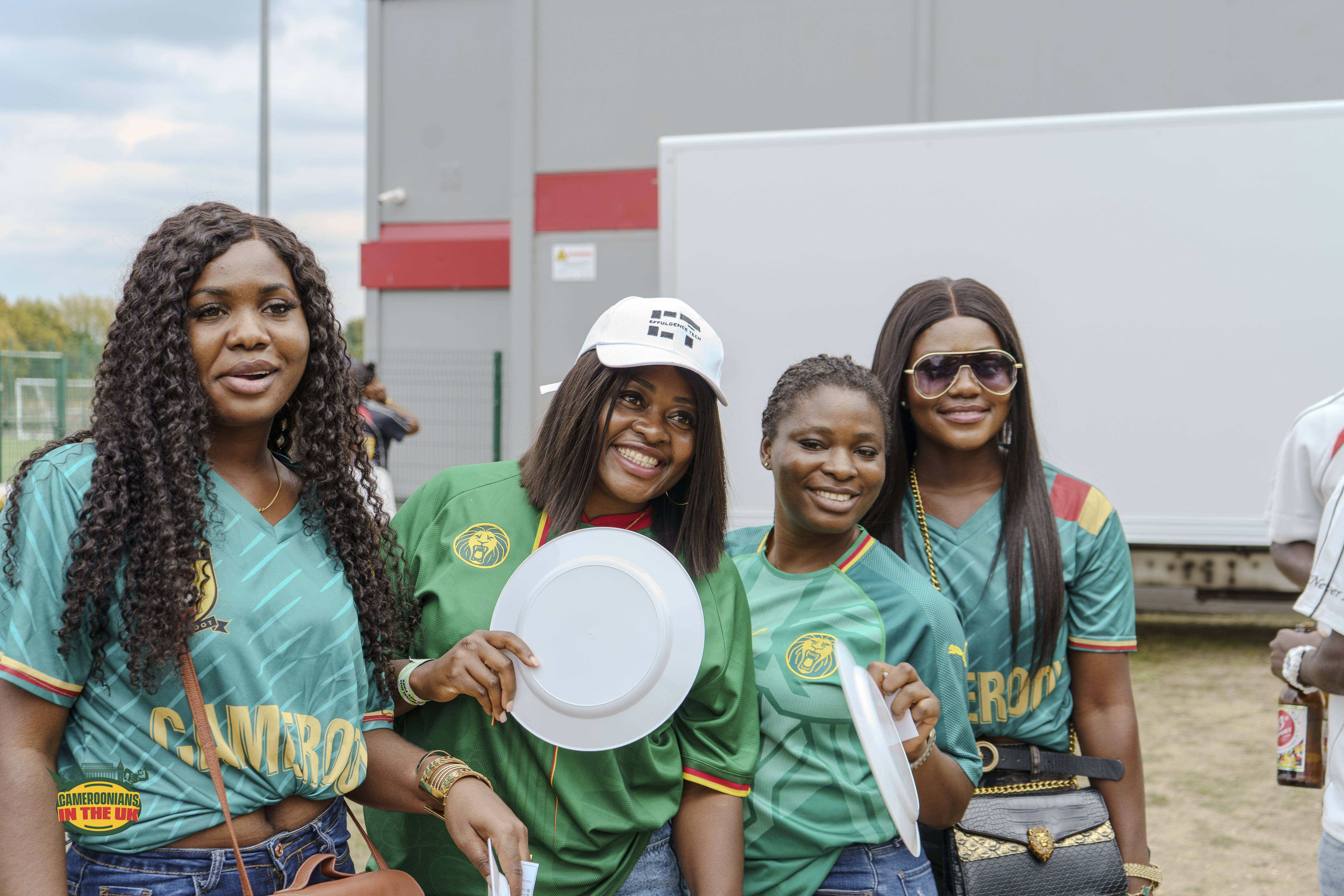 Four CAMUK members in Cameroon football shirts at a community event